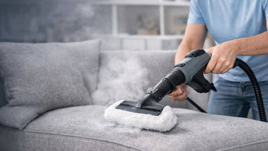 Nettoyeur vapeur en train de nettoyer un canapé en tissu gris avec vapeur visible pour un nettoyage en profondeur